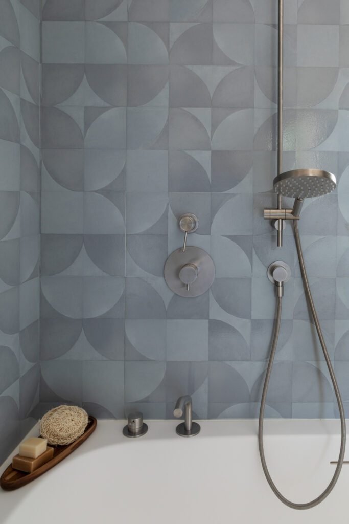parete vasca con piastrelle azzurro-grigio e rubinetteria in acciaio inox